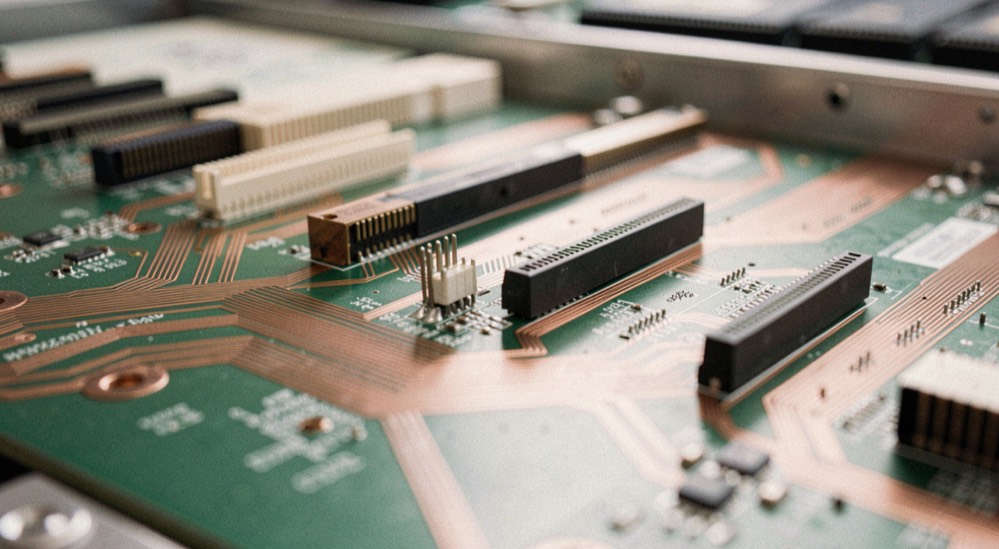 Close view of a server backplane with several edge connectors of different lengths lit from the side, copper traces fanning out across the green board
